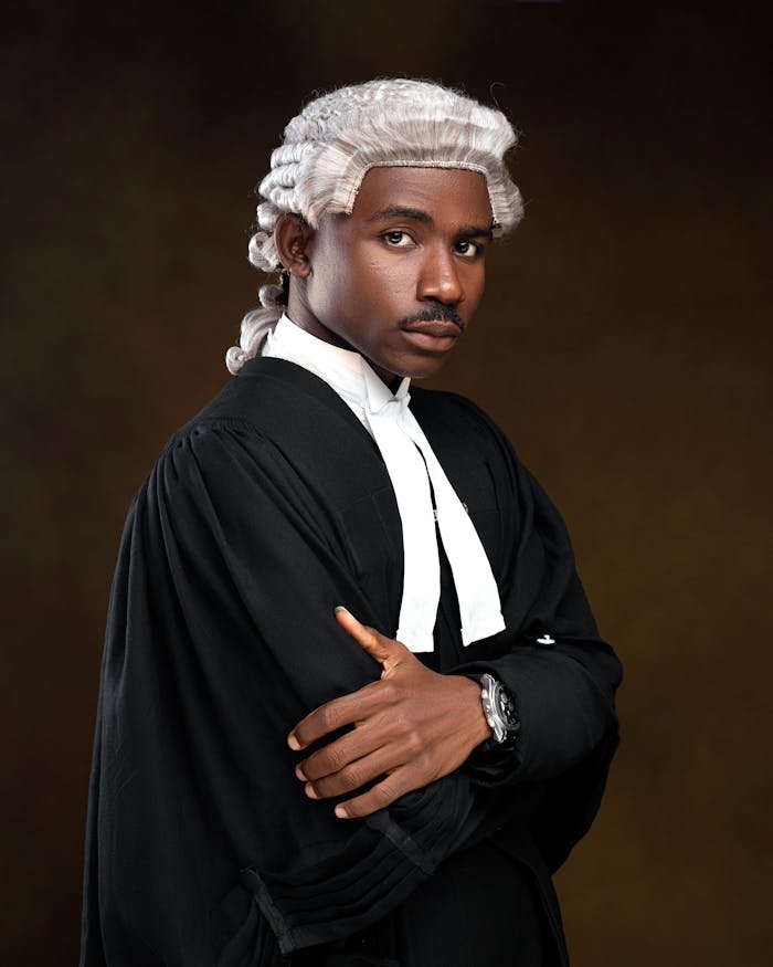 Portrait of a confident lawyer wearing traditional attire and wig, with arms crossed.